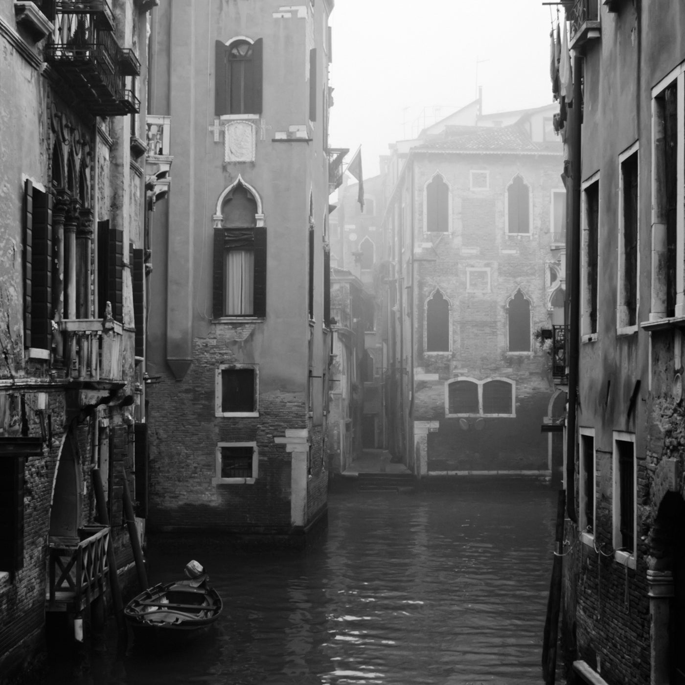 Canale veneziano in bianco e nero con gondola e architettura storica, atmosfera nebbiosa